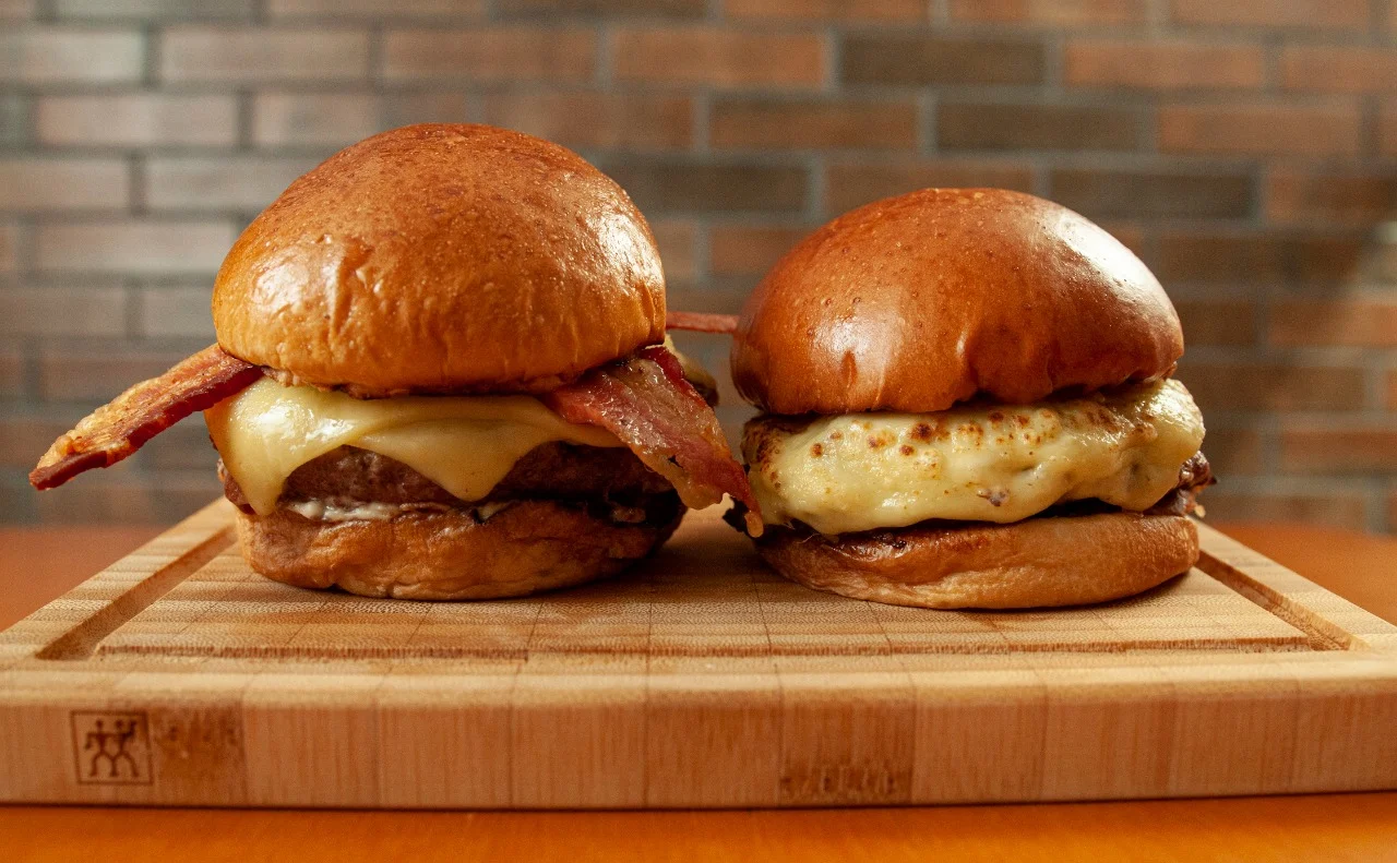 Dois hambúrgueres com queijo e bacon sobre uma tábua — fotografia de Ulysses Paiva para Dom Ferreira Forneria